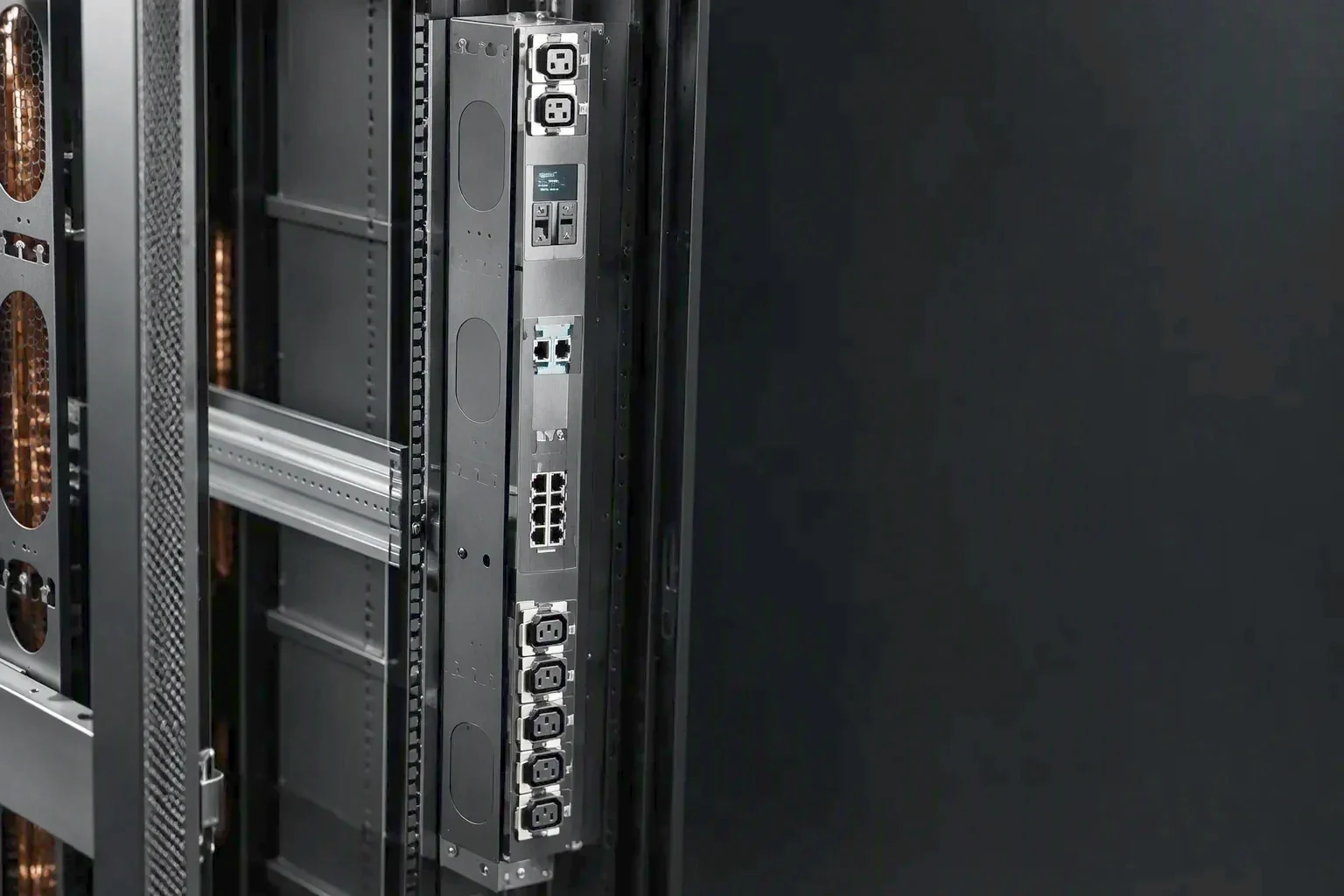 Production station and equipment detail on the enclosure line, a rack PDU chassis staged in three-quarter view in the left of the frame while a single raking light falls across the brushed steel