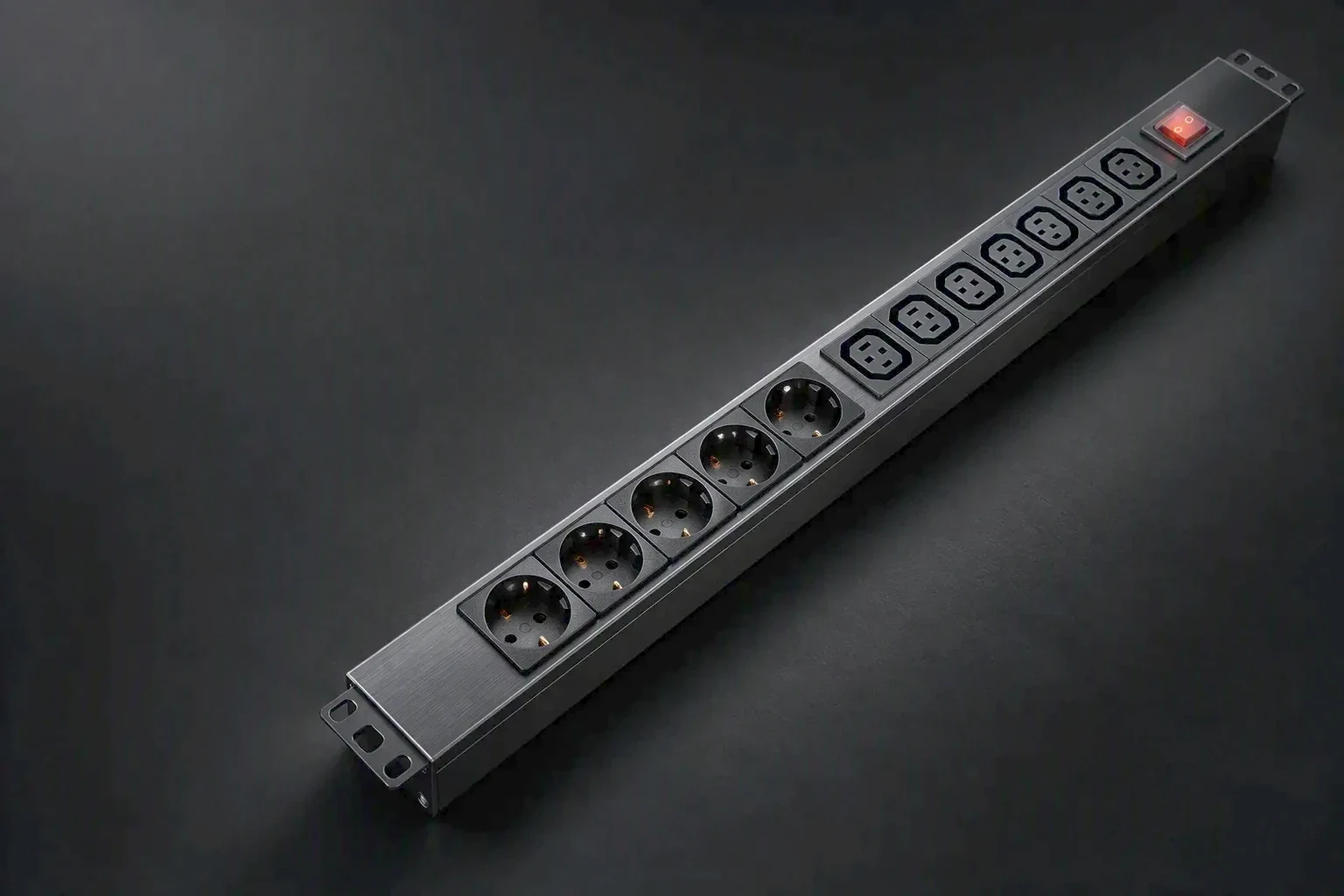 A rack power distribution unit lit by one raking light across a brushed steel face, the left two thirds held in shadow