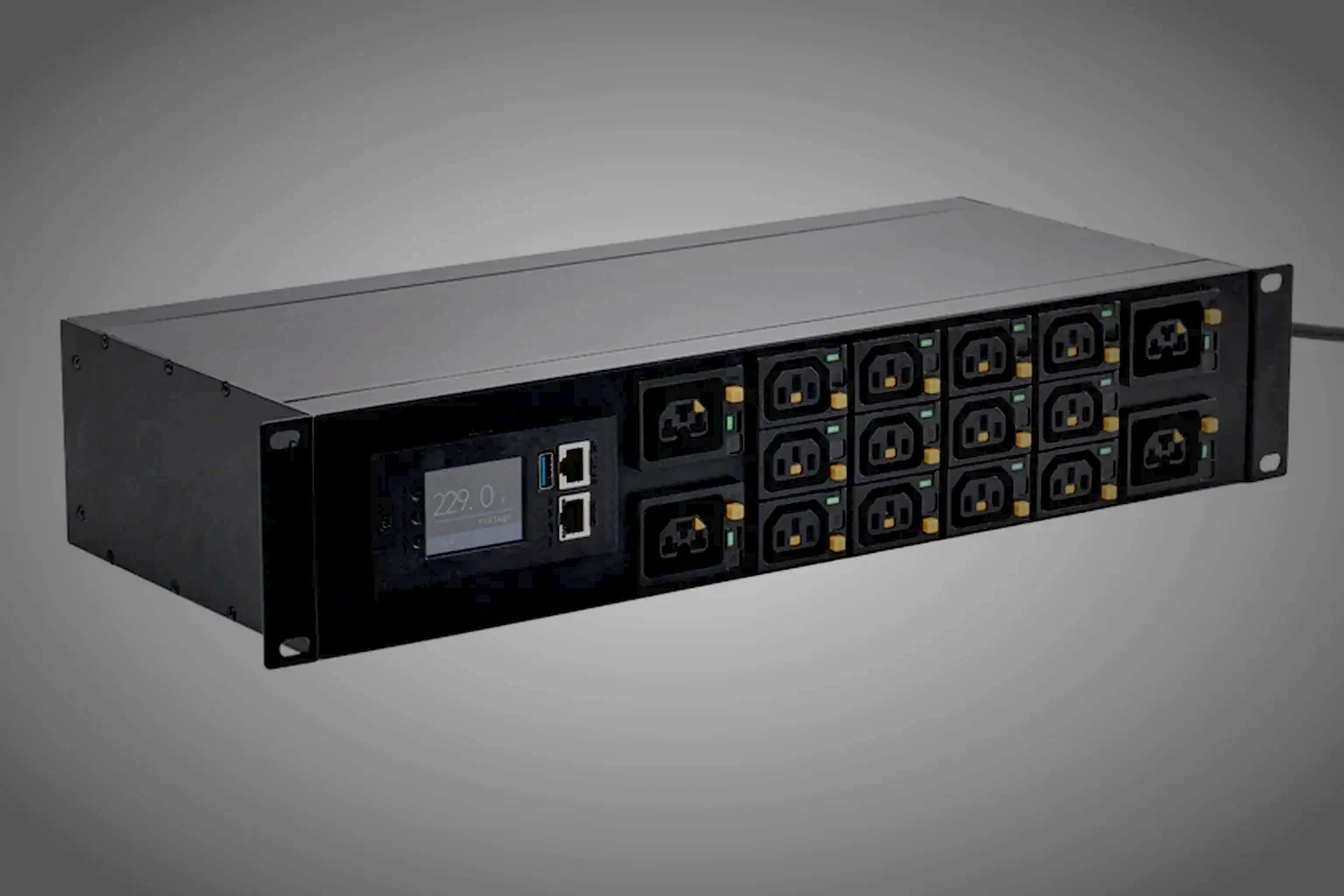 A rack PDU held in the right of the frame at a low three-quarter angle, its readout panel lit warm orange above the outlet rank with the left of the frame left as clean unlit space