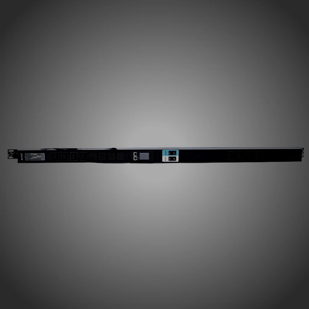 A rack PDU held at the left of the frame in a dark equipment aisle, one raking light along its brushed steel body with the rack behind it out of focus