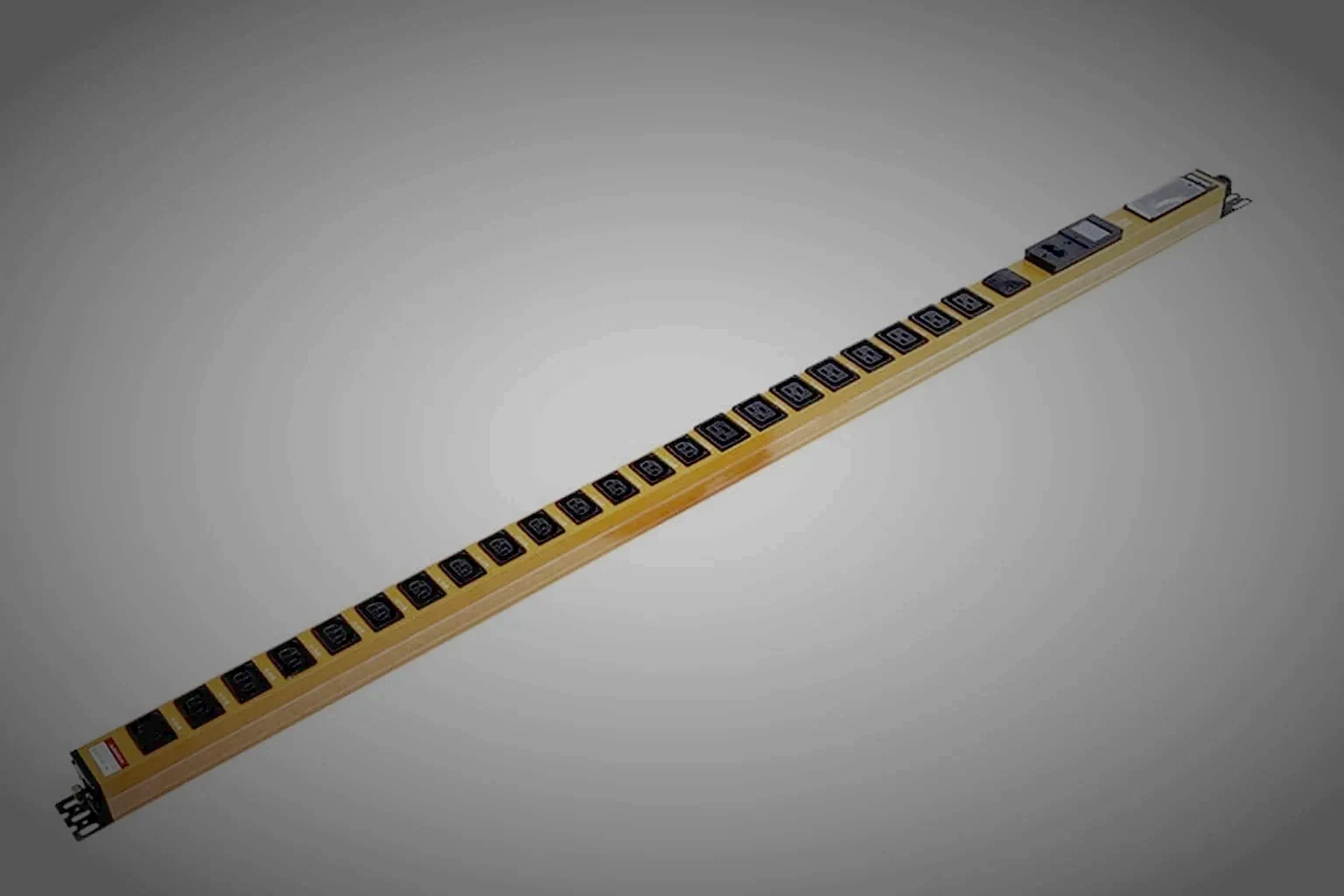 A rack PDU held in the right of the frame at a low three-quarter angle, a small display glowing warm orange on its brushed steel face while the left of the frame falls into unlit dark