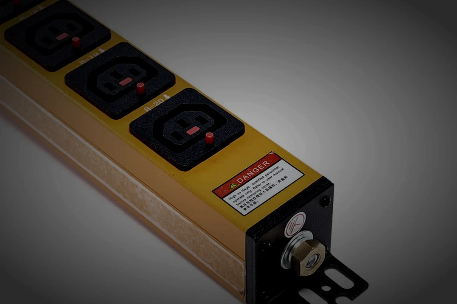 A metered rack PDU seen from a raised three-quarter angle with its OLED display lit faintly in warm orange, one raking light along the brushed steel face, the unit held in the right of the frame and the left third in unlit dark