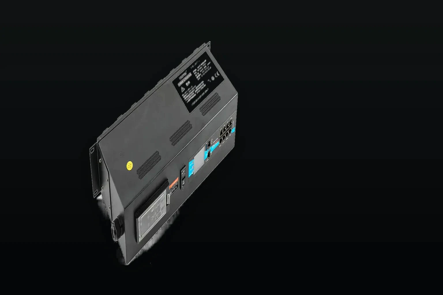 Electrical test bench under one raking light: a unit clamped in its fixture at the left of the frame with current meters and a load bank beside it, the right side falling into unlit dark